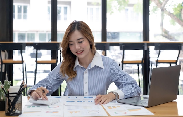 Mulher de negócios asiática usando computador portátil e trabalhando no escritório com documento de calculadora na mesa fazendo planejamento analisando o conceito de análise de finanças de investimento de plano de negócios de relatório financeiro