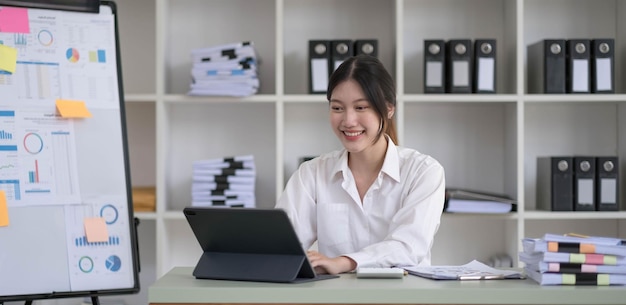 Mulher de negócios asiática usando computador portátil e trabalhando no escritório com documento de calculadora na mesa fazendo planejamento analisando o conceito de análise de finanças de investimento de plano de negócios de relatório financeiro