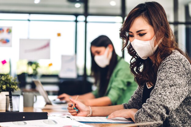 Mulher de negócios asiática usando laptop com máscara facial no escritório