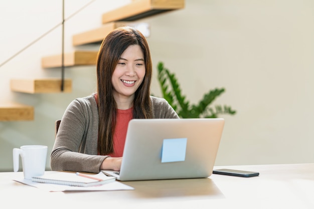 Mulher de negócios asiática usando laptop e celular de tecnologia para trabalhar em casa