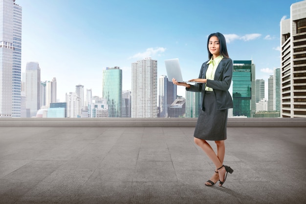 Mulher de negócios asiático em pé enquanto estiver usando um laptop