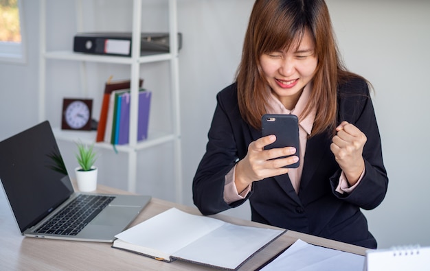 Mulher de negócios asiático parece feliz enquanto olha para as informações no telefone