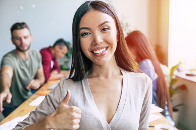 Mulher de negócios asiáticos bonita confiante jovem feliz em smart casual wear está posando em fundo de equipe de negócios modernos. Colegas de trabalho. Equipe inicial. Alunos juntos