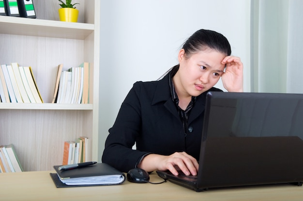 Mulher de negócios asiáticos de dor de cabeça, segurando a cabeça dela, trabalhando com laktop