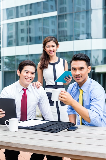 Mulher de negócios asiáticos e homens trabalhando ao ar livre no computador tomando café