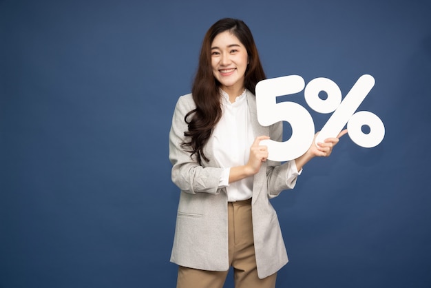 Mulher de negócios asiáticos mostrando e segurando o número de 5% ou cinco por cento isolado sobre a superfície de um azul profundo.