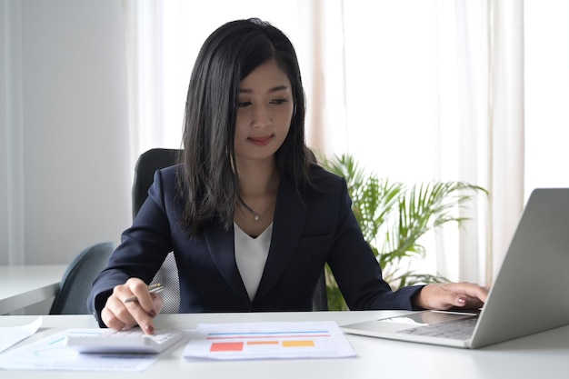 Mulher de negócios asiáticos usando calculadora e trabalhando com laptop na mesa de escritório