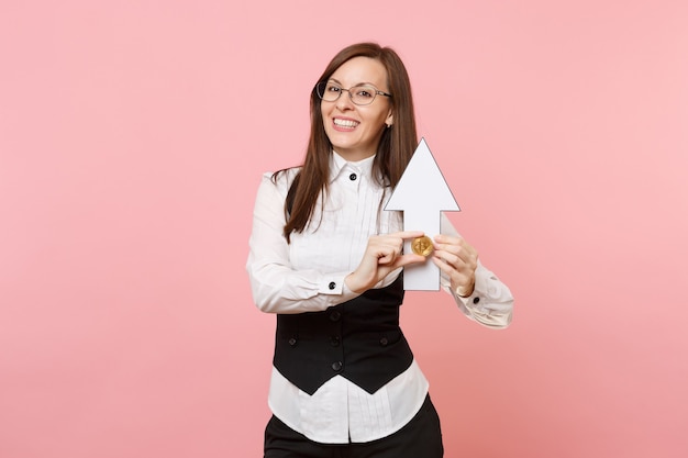 Mulher de negócios atraente alegre jovem em terno preto, óculos segurando bitcoin, seta para cima isolada em fundo rosa pastel. Senhora chefe. Conceito de riqueza de carreira de conquista. Copie o espaço para anúncio.