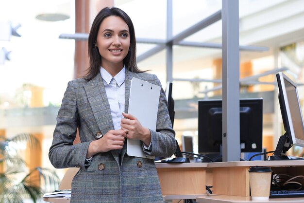 Mulher de negócios atraente em pé perto da mesa no escritório.