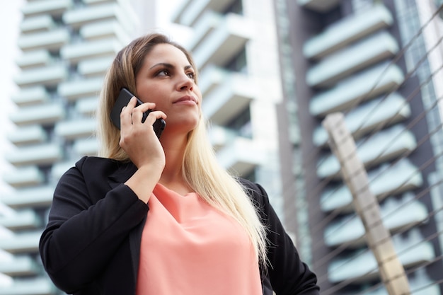 Mulher de negócios atraente falando para celular em ambiente urbano