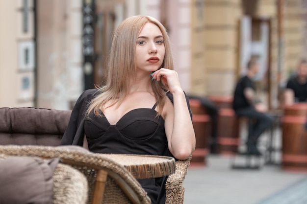 Mulher de negócios atraente jovem sentada à mesa no café de rua em terno preto e esperando seu pedido Mulher solitária