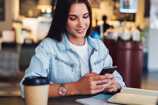 Foto mulher de negócios atraente se senta à mesa em frente ao laptop e fala no celular, negocia ao telefone.