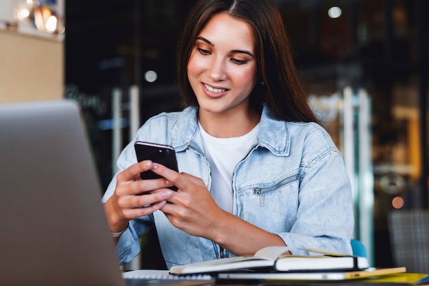 Mulher de negócios atraente se senta à mesa em frente ao laptop e fala no celular, negocia ao telefone.