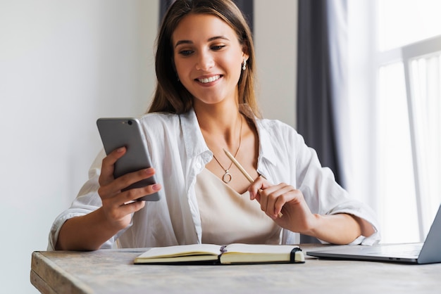 Mulher de negócios atraente se senta à mesa em frente ao laptop e fala no celular, negocia ao telefone.