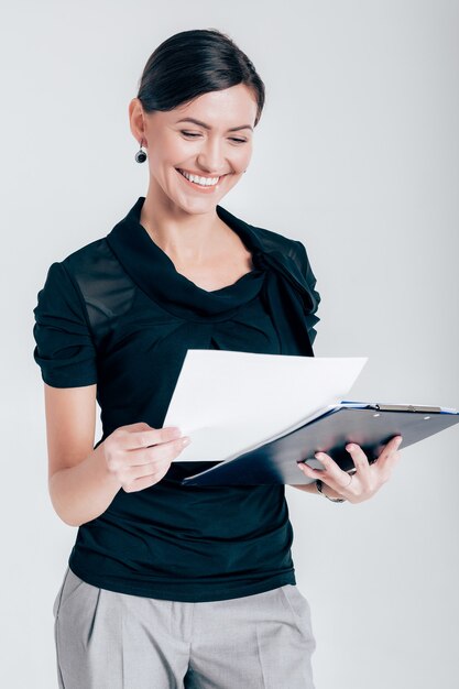 Mulher de negócios atraente sorridente segurando uma pasta com documentos em um fundo cinza