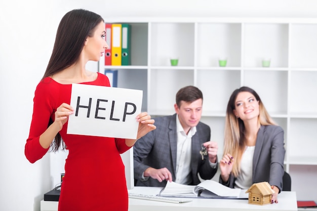 Mulher de negócios atraente, triste e desesperada, sofrendo de estresse na mesa do computador laptop do escritório segurando um cartaz de ajuda