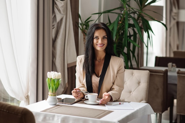 Mulher de negócios bem-sucedida está bebendo café durante o dia de trabalho no café