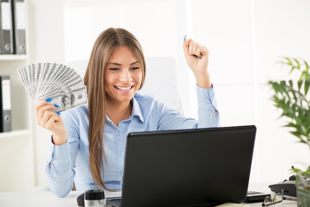 Mulher de negócios bem sucedida feliz no escritório que guarda o dinheiro com braços aumentados.