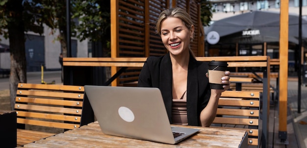 Mulher de negócios bem-sucedida jovem trabalhando com laptop e tomando café ao ar livre