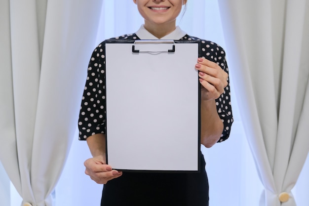 Mulher de negócios bem-sucedida sorridente madura mostrando o papel em branco na área de transferência. dona de casa perto da janela, lugar para seu texto, espaço de cópia