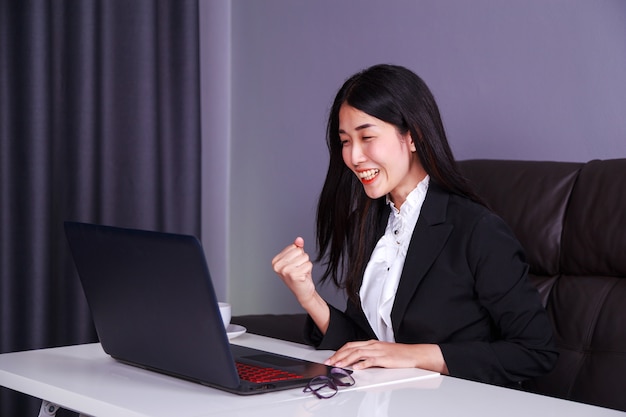 Mulher de negócios bem sucedido, levantando o braço em felicidade com o computador portátil