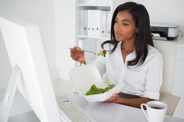 Mulher de negócios bonita comendo uma salada na mesa dela