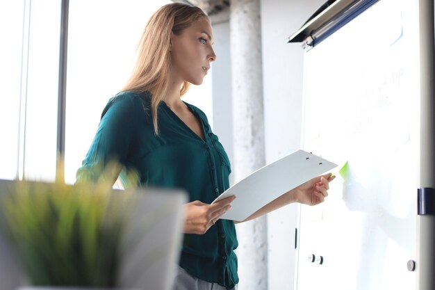 Mulher de negócios bonita está perto do flipchart e examinando informações nele.