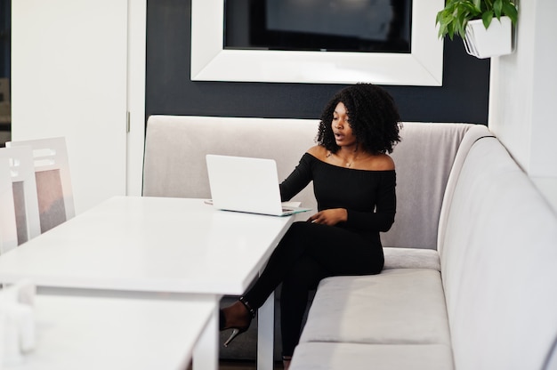 Mulher de negócios bonita jovem elegante com penteado afro, sentado e trabalhando no laptop