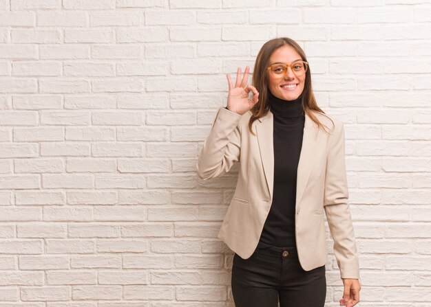 Mulher de negócios bonita jovem empreendedor alegre e confiante, fazendo o gesto de ok