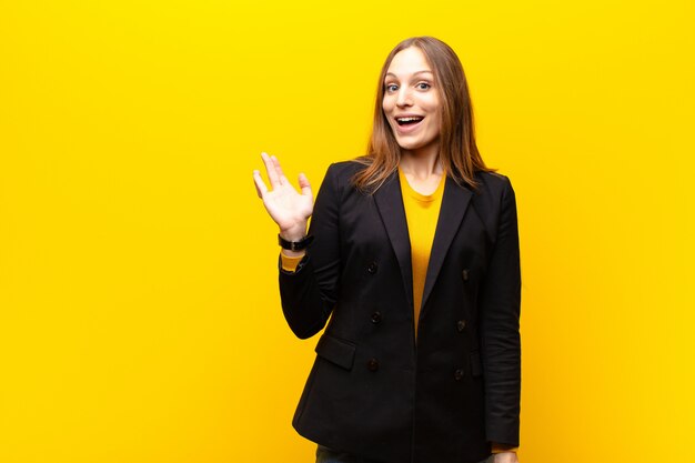 Mulher de negócios bonita nova que sente feliz, surpreendida e alegre, sorrindo com atitude positiva, realizando uma solução ou uma ideia contra a laranja