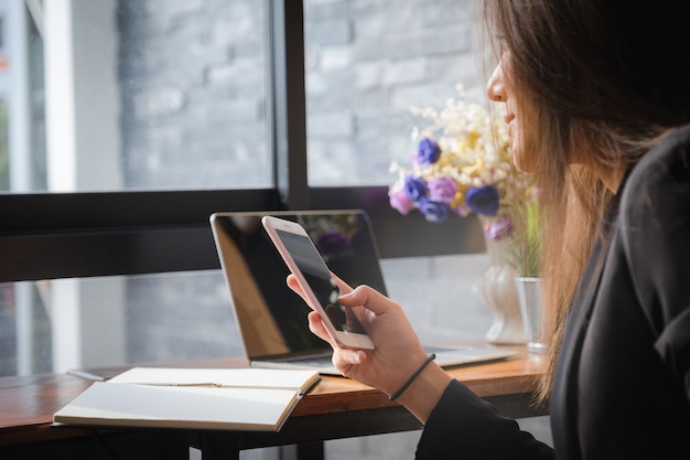 Mulher de negócios bonita que usa o dispositivo do smartphone nas mãos.