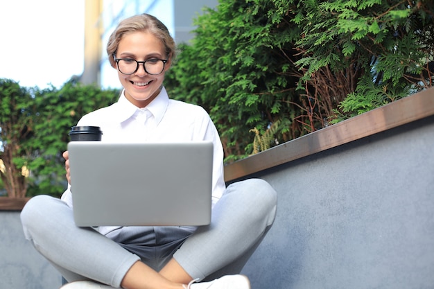 Mulher de negócios bonita sentada perto do centro de negócios e usando o laptop.