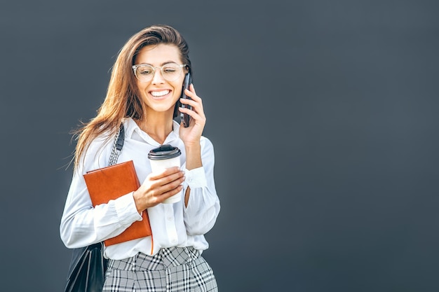 Mulher de negócios, caminhando e falando no celular ao ar livre, perto do moderno centro de negócios com notebook.