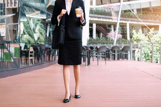 Mulher de negócios, caminhando e segurando a xícara de café fora do escritório