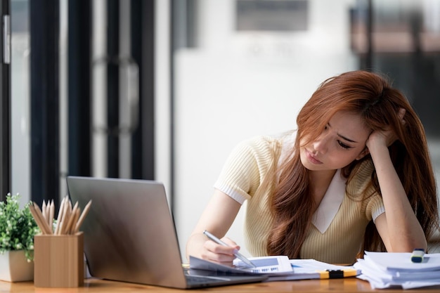 Mulher de negócios cansada com sono e entediada do trabalho sentada em uma mesa por um longo tempo e tem síndrome de escritório