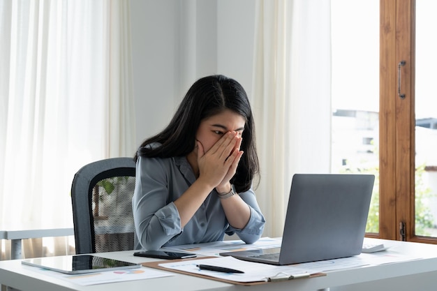 Mulher de negócios cansada em estresse trabalha em um laptop enquanto está sentado em uma mesa em casa e segura a mão em seus templos ataque de enxaqueca Trabalho freelance em casa