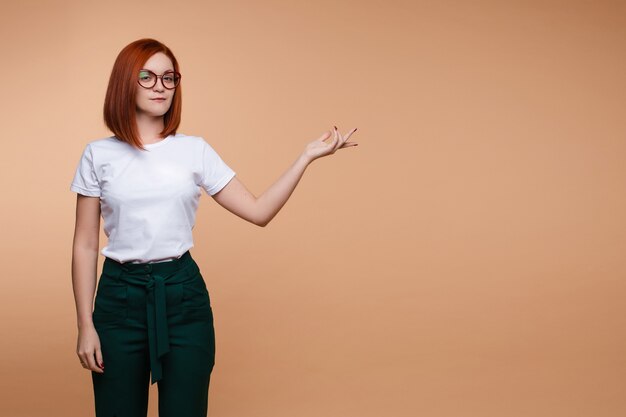 Mulher de negócios casuais em copos, mostrando a mão isolada no fundo do estúdio. mulher ruiva sorridente apontando para um texto posando olhando para a câmera