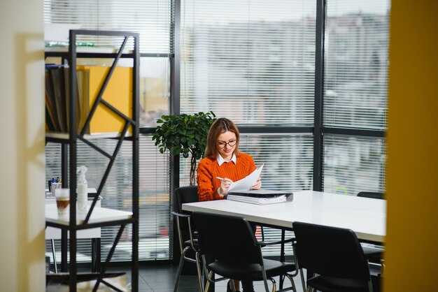 Mulher de negócios casual com suéter sentada em sua mesa no escritório