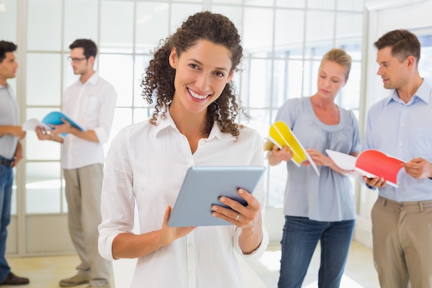 Mulher de negócios casual usando um tablet com o time atrás dela