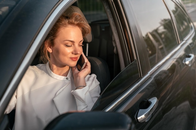 Mulher de negócios caucasiana confiante falando no celular sentado no carro. Conceito de transporte