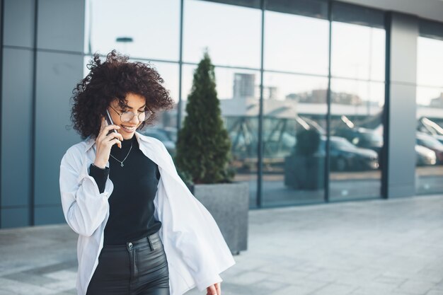 Mulher de negócios caucasiana de cabelos cacheados caucasiana falando no telefone com um empresário do lado de fora em uma camisa branca