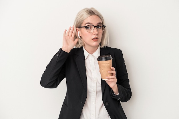 Mulher de negócios caucasiana jovem segurando tomar café isolado no fundo branco, tentando ouvir uma fofoca.