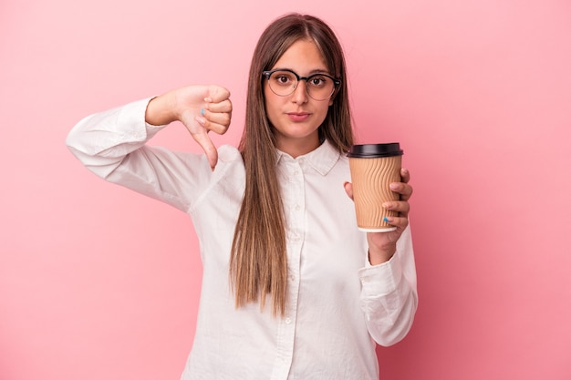 Mulher de negócios caucasiana jovem segurando um take away isolado no fundo rosa, mostrando um gesto de antipatia, polegares para baixo. Conceito de desacordo.