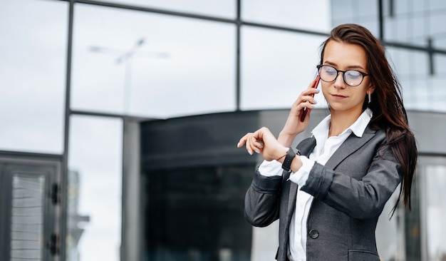 Mulher de negócios checa as horas e fala ao telefone na cidade durante um dia de trabalho