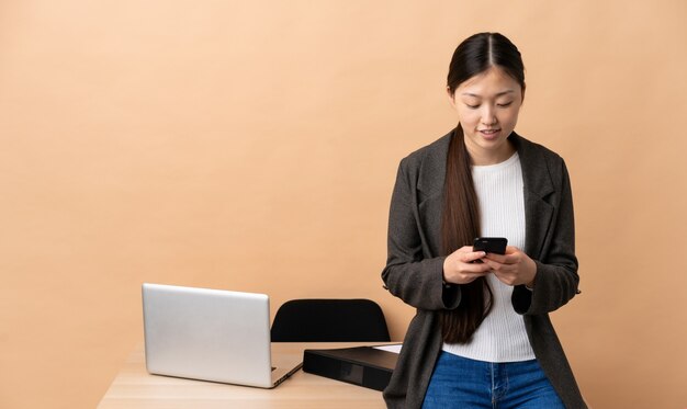 Mulher de negócios chinês em seu local de trabalho, enviando uma mensagem com o celular