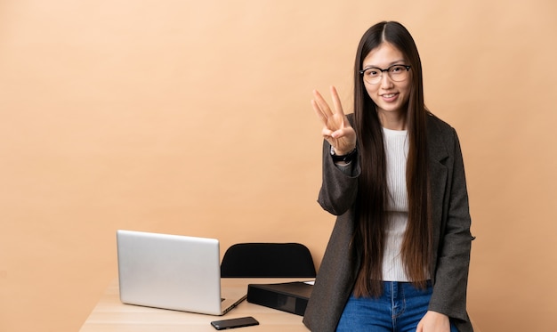 Mulher de negócios chinês em seu local de trabalho feliz e contando três com os dedos