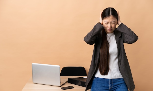 Mulher de negócios chinês em seu local de trabalho frustrado e cobrindo as orelhas
