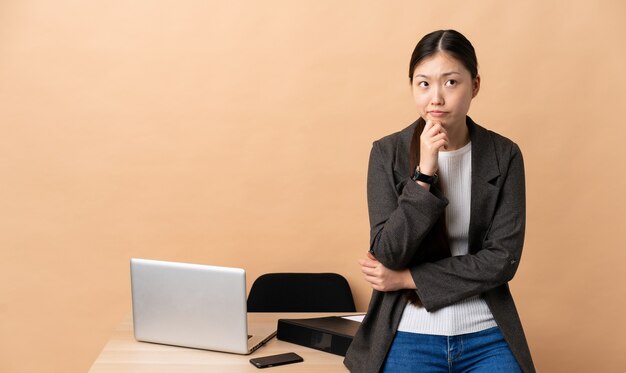 Mulher de negócios chinesa em seu local de trabalho, tendo dúvidas e pensando