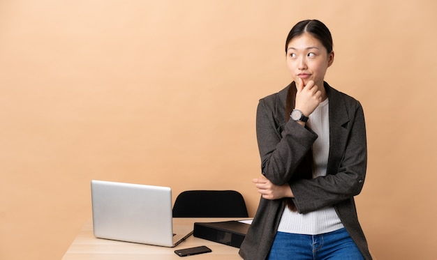 Mulher de negócios chinesa no local de trabalho, pensando uma ideia enquanto olha para cima