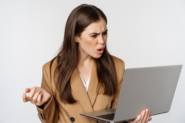 Mulher de negócios chocada e decepcionada olhando para a tela do laptop com rosto frustrado ofendido expre...